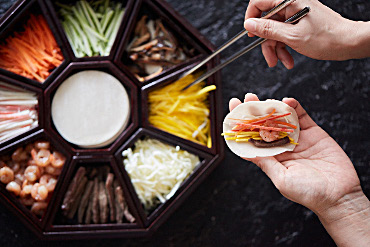Hands using chopsticks to pick up food from a dish full of various cut foods